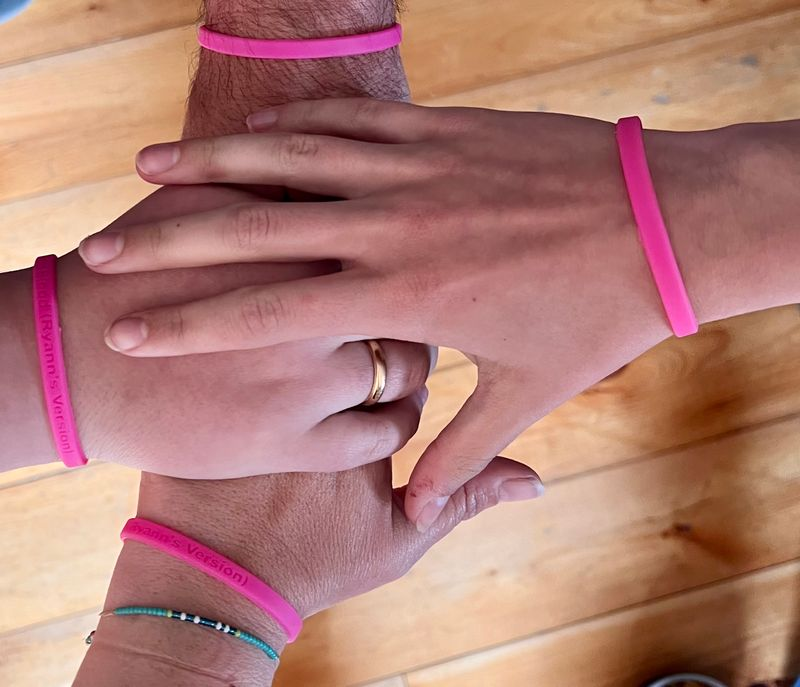 four stacked hands wearing pink wristbands